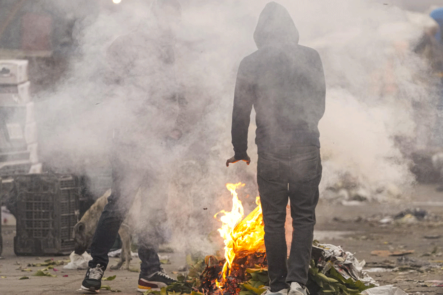 People warm themselves by a small fire as cold weather conditions prevail, at Sahibabad Sabzi Mandi, in Ghaziabad.