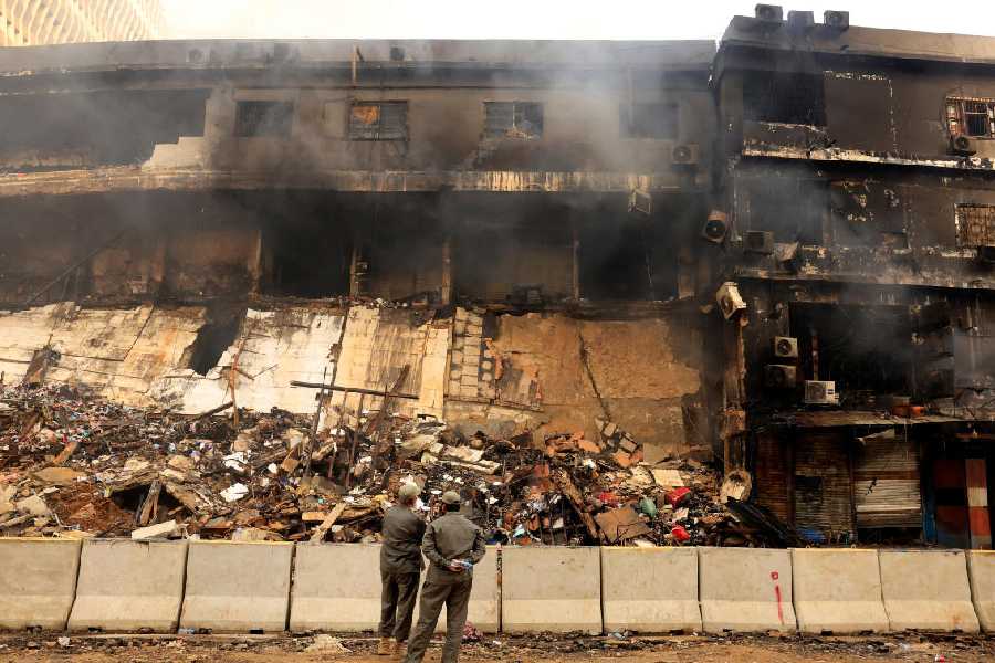 Members from Karachi Municipal Corporation watch as smoke rises from a smoldering building in the Gul Plaza Shopping Centre