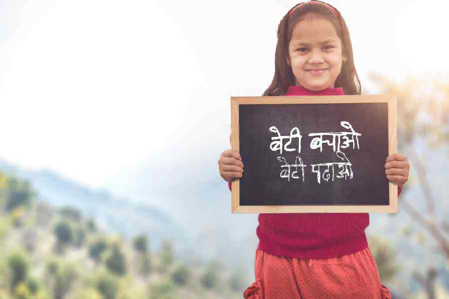Adorable little 6-8 years old Indian girl smiling, holding beti bachao beti padhao chalkboard.
