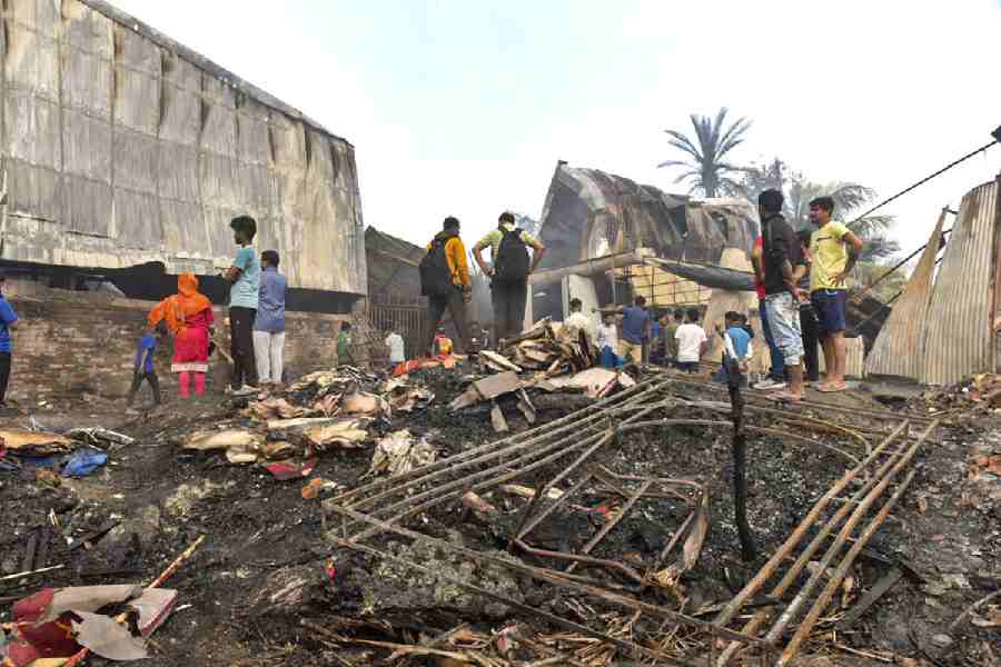 People gather near the charred remains of a fire at a warehouse, in Kolkata, Monday, Jan. 26, 2026. A fire broke out in a warehouse in the Nazirabad area of Anandapur, Kolkata, in the early hours of Monday, causing at least seven feared deaths and multiple missing persons.