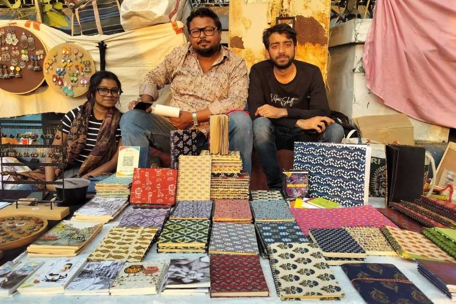 Around 20 to 25 artisans sit on the pavement, displaying handmade notebooks, home decor items, jewellery, paintings, itar and bookmarks on Tarpaulins laid out on footpaths