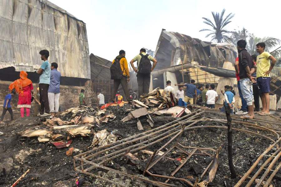 People gather near the charred remains of a fire at a warehouse, in Kolkata, Monday, Jan. 26, 2026.