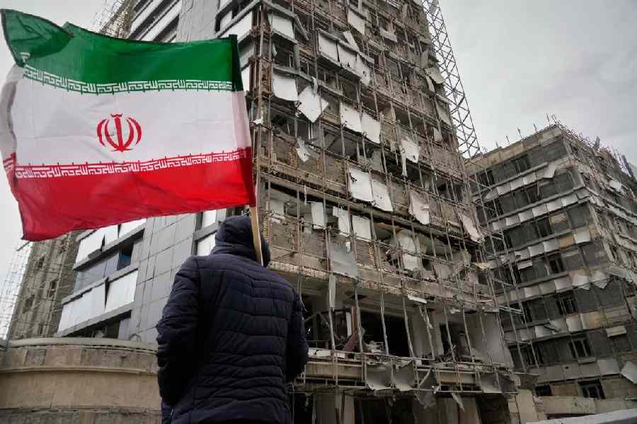 A man holds an Iranian flag as he looks at the damaged Gandhi Hospital in Tehran, Iran, which was hit on Sunday