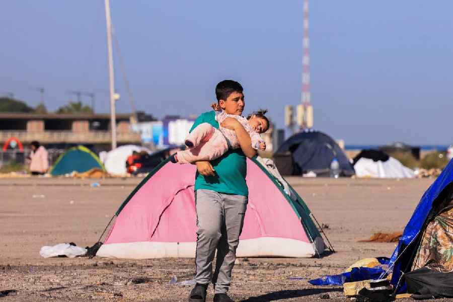A displaced boy carries a child near tents, following an escalation between Hezbollah and Israel, amid the U.S.-Israeli conflict with Iran, in Beirut, Lebanon