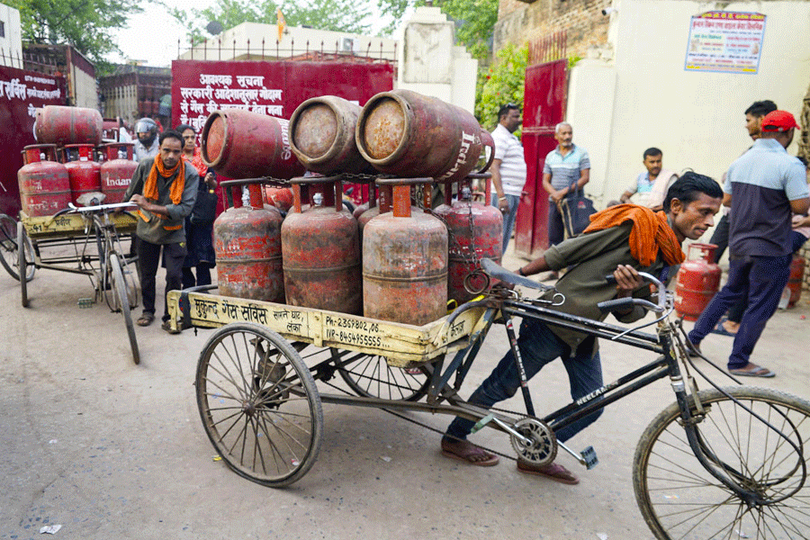 A worker carries LPG cooking gas cylinders, as people arrive to avail refilled ones, amid a shortage linked to the ongoing West Asia conflict affecting the global energy supply chain, in Varanasi, Wednesday, March 18, 2026.