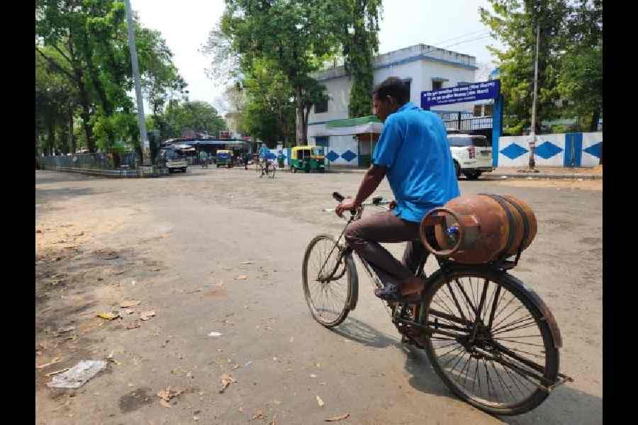 A man cycles with a cylinder strapped behind, in AG Block.