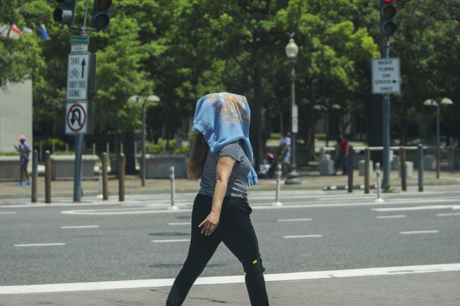 A woman wearing a sweatshirt on her head to protect herself from the sun walks across a crosswalk in downtown Washington, Wednesday, June 19, 2024. High temperatures are expected to stay in the 90s in the nation's capital for the rest of the week as a heat wave builds into the Northeast.
