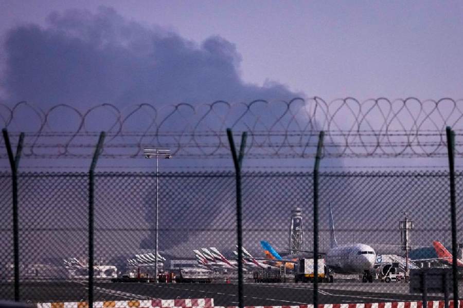 Planes are parked at Dubai International Airport as smoke rises in the background after a drone struck a fuel tank early morning, forcing the temporary suspension of flights, in Dubai, United Arab Emirates, Monday, March 16, 2026