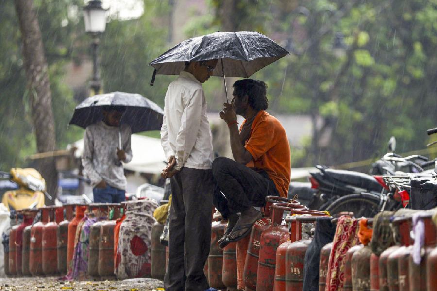 Men wait with empty LPG cylinders amid rainfall during an ongoing supply crisis, in Prayagraj
