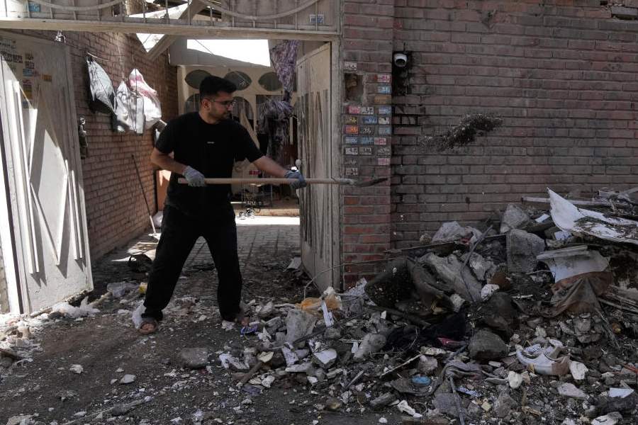 A man clears debris from a building damaged after a nearby residential building was hit in a U.S.-Israeli strike in Tehran, Friday, March 27, 2026.