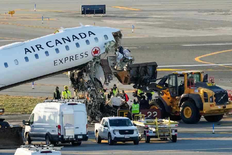 Workers position a front loader under debris hanging from the wreckage of the Air Canada Express jet at LaGuardia on March 24.