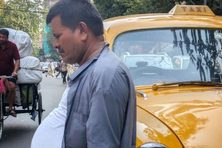 A taxi driver waits under the shade beside his cab during the afternoon heat