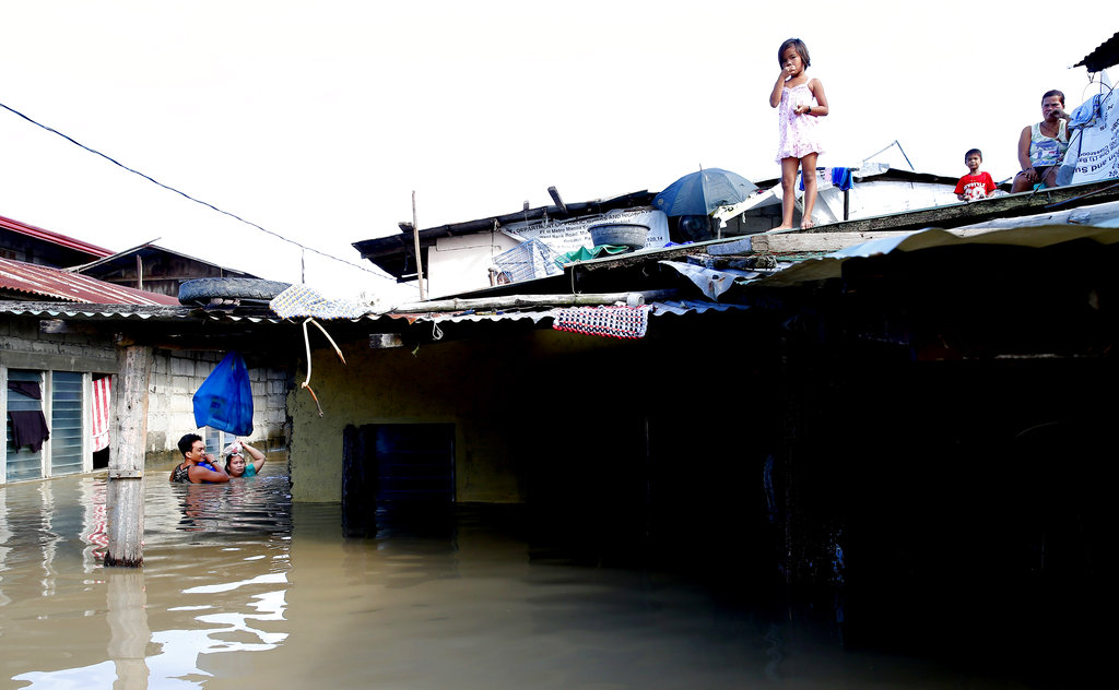 A couple wades through water as a girl watches from a rooftop following flooding brought about by Typhoon Mangkhut, which barreled into northeastern Philippines.