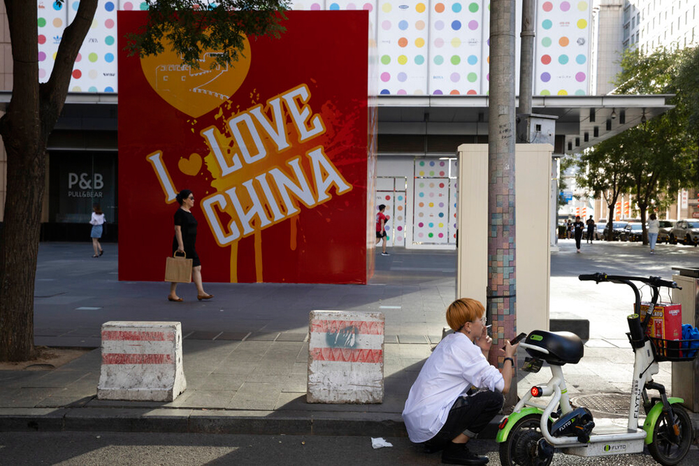 A resident smokes near a board with the words 'I Love China' at a retail district in Beijing