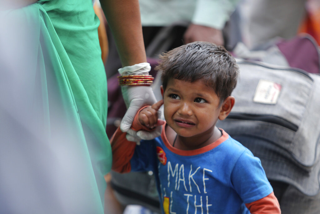 A migrant worker's child waits with an adult outside a railway station hoping to be able to travel to their home states, in Jammu, ,on Friday, May 22, 2020.