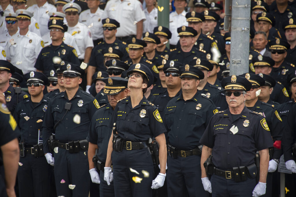 Honolulu Police Chief Susan Ballard, middle, looks up as Honolulu Fire Department and HPD helicopters drop flowers onto a procession for police Officer Tiffany-Victoria Enriquez, on Thursday