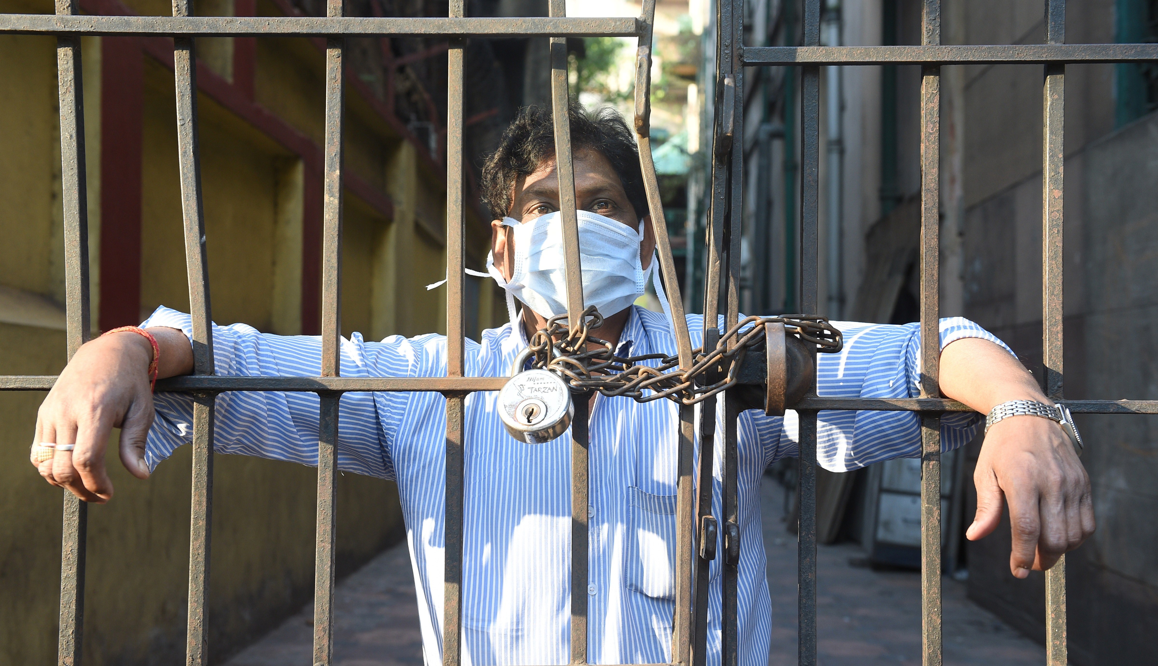 A man, wearing a mask, looks from a closed gate during lockdown in the wake of coronavirus pandemic, in Calcutta, Tuesday, March 24, 2020