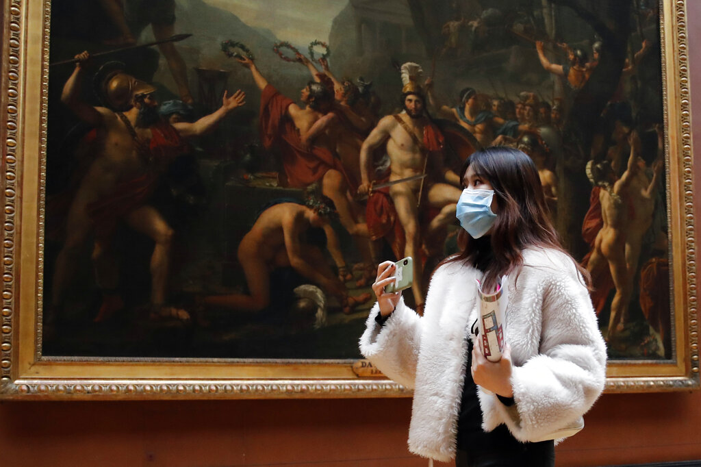 Masked tourist walks by an oil on canvas of 1814 entitled Leonidas at Thermopylae, by Jacques Louis David, at the Louvre Museum in Paris, Thursday, March 5, 2020. With the COVID-19 virus taking firmer hold in Europe, the continent is facing the same complications seen in Asia weeks ago.