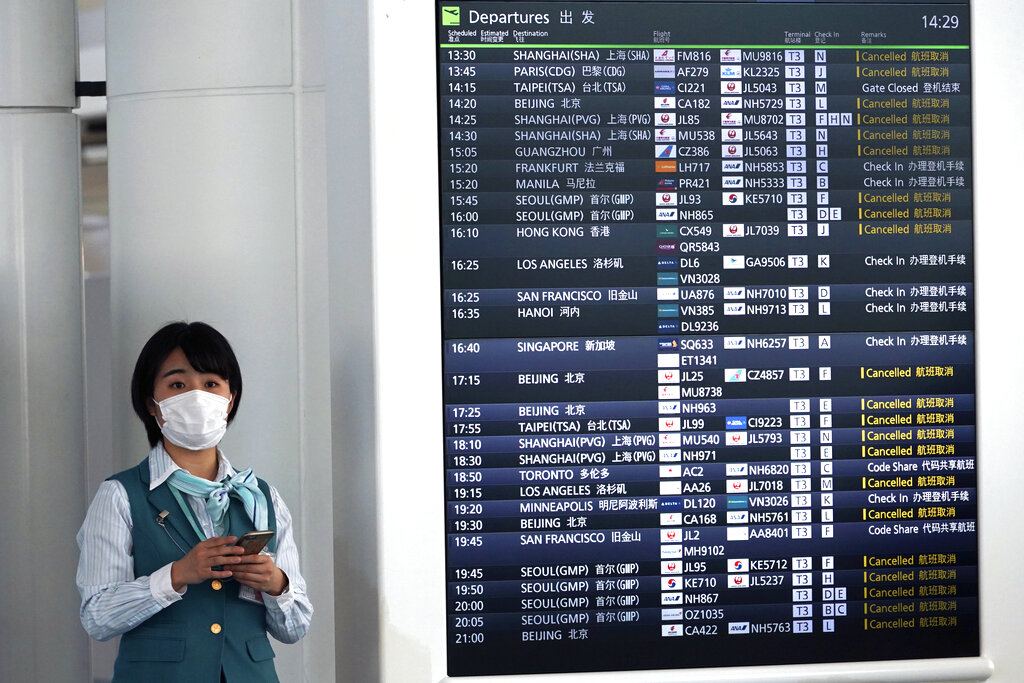 Airline staff stands next to a flight schedule board showing numerous canceled flights due to the coronavirus at the Haneda International Airport in Tokyo, Wednesday, March 18, 2020.
