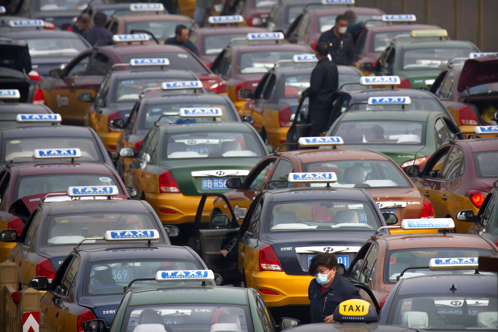 A taxi driver wearing a face mask stands in the taxi queue at the Beijing Railway Station in Beijing, Wednesday, March 25, 2020.
