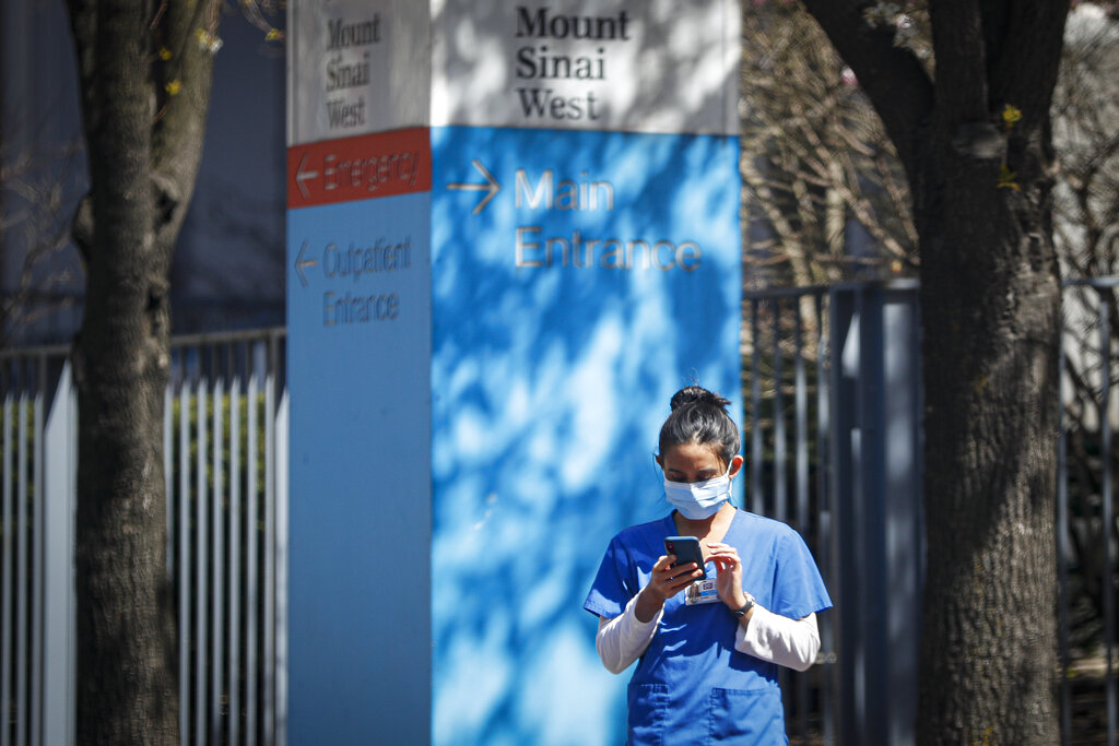 A medical worker uses her phone while wearing a surgical mask outside Mt. Sinai West, Thursday, March 26, 2020, in New York.