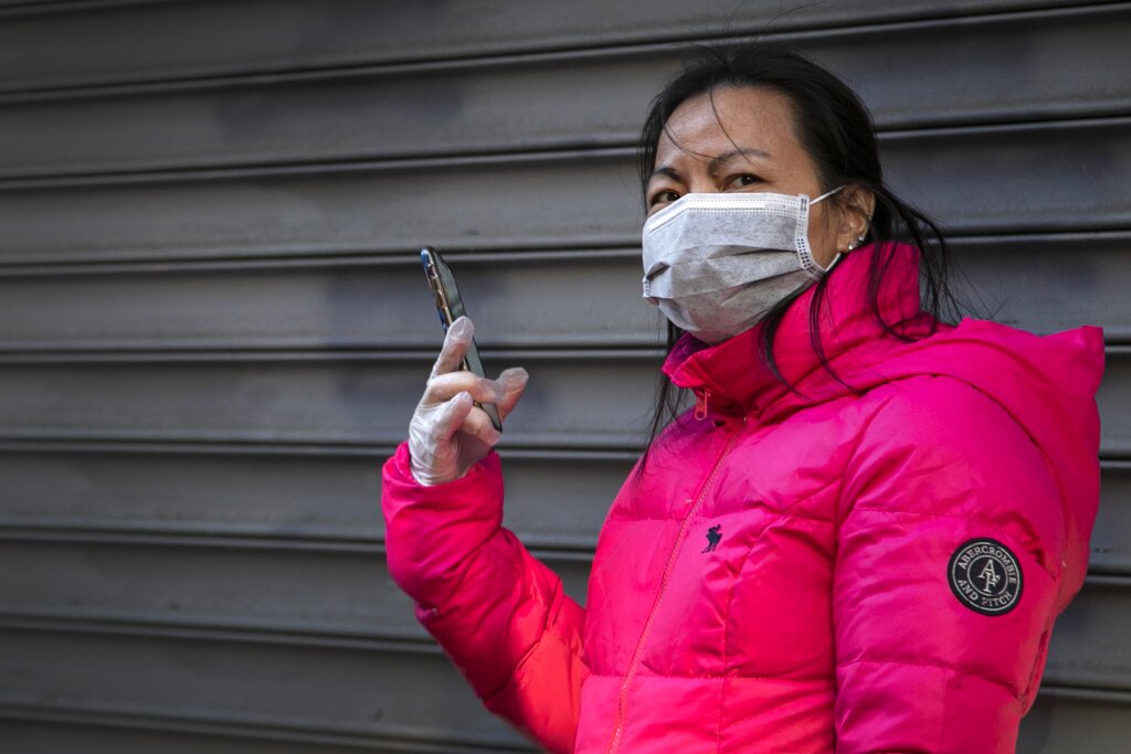 A woman wears surgical gloves and a face mask as she speaks on her smart phone in Chinatown on Sunday, March 15, 2020, in New York.