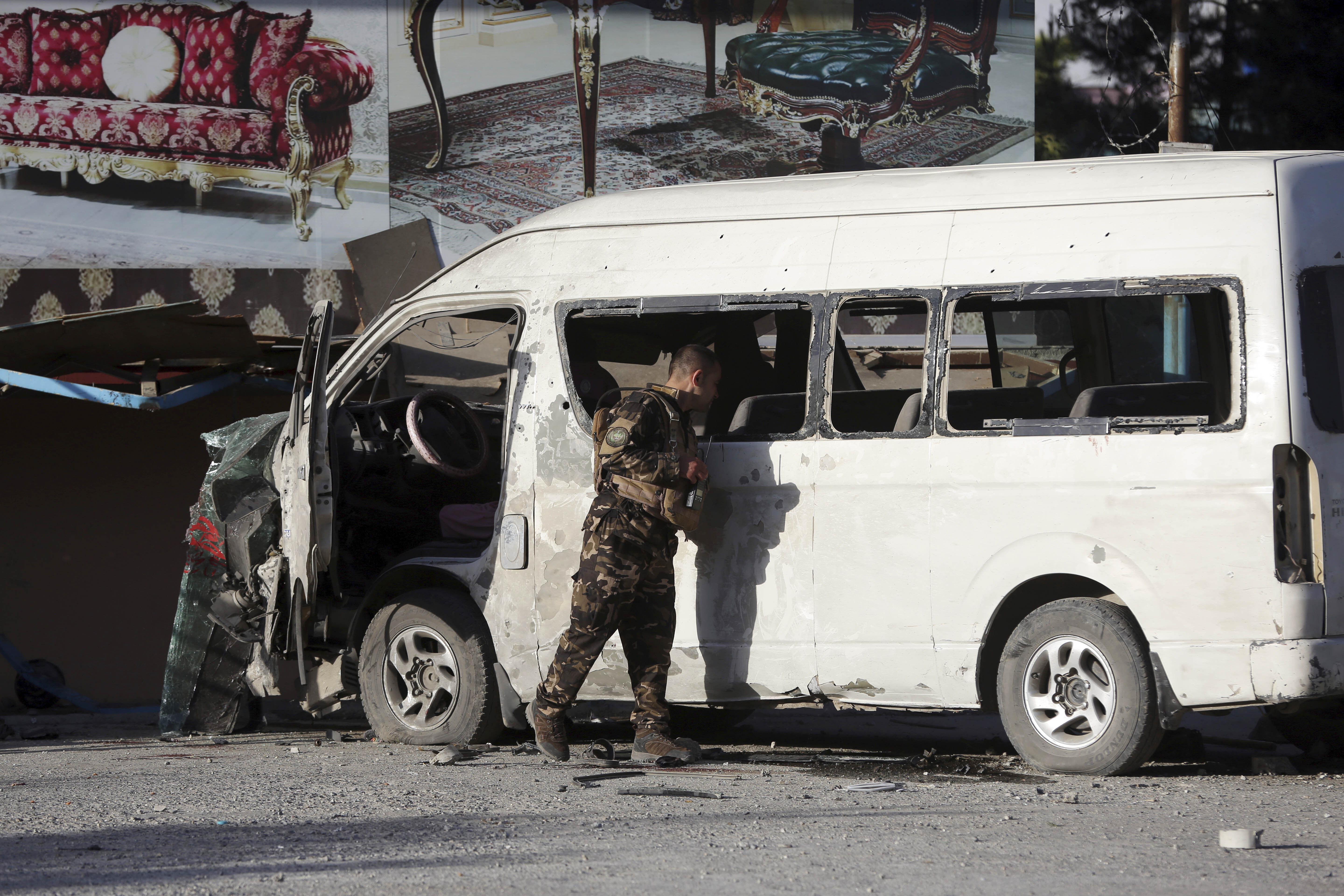 An Afghan security forces member inspects a bus carrying local TV station employees that hit a roadside bomb in Kabul