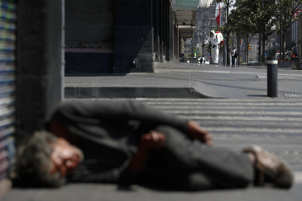 A city worker sprays disinfectant as a man sleeps on the street, in central Mexico City, on Monday. Mexican President Andres Manuel Lopez Obrador said Sunday there will be no huge economic stimulus program as the country faces the threat of coronavirus-induced crisis almost certainly unlike any it has seen in the past century.