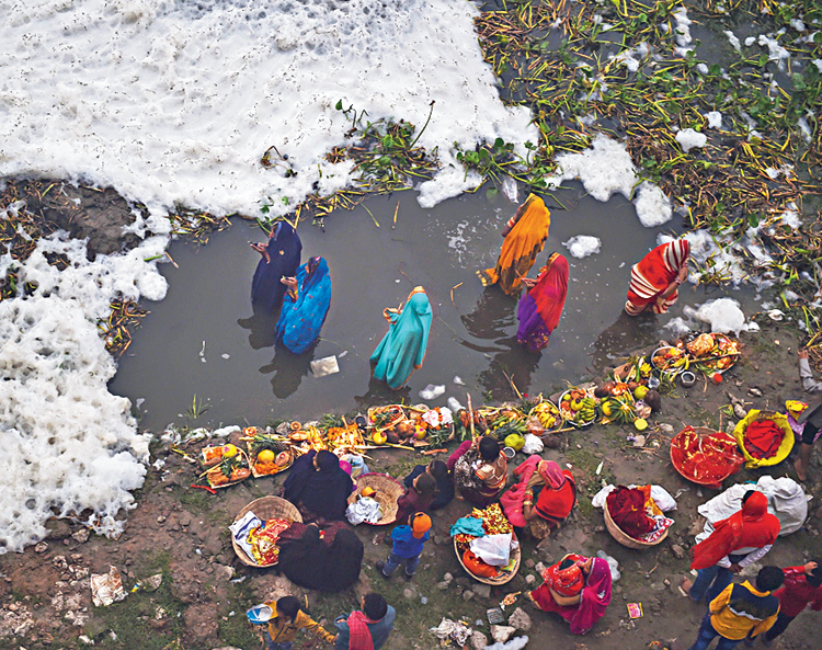 Devotees offer prayers as toxic foam floats on the Yamuna river during the Chhath Puja in New Delhi on November 3, 2019