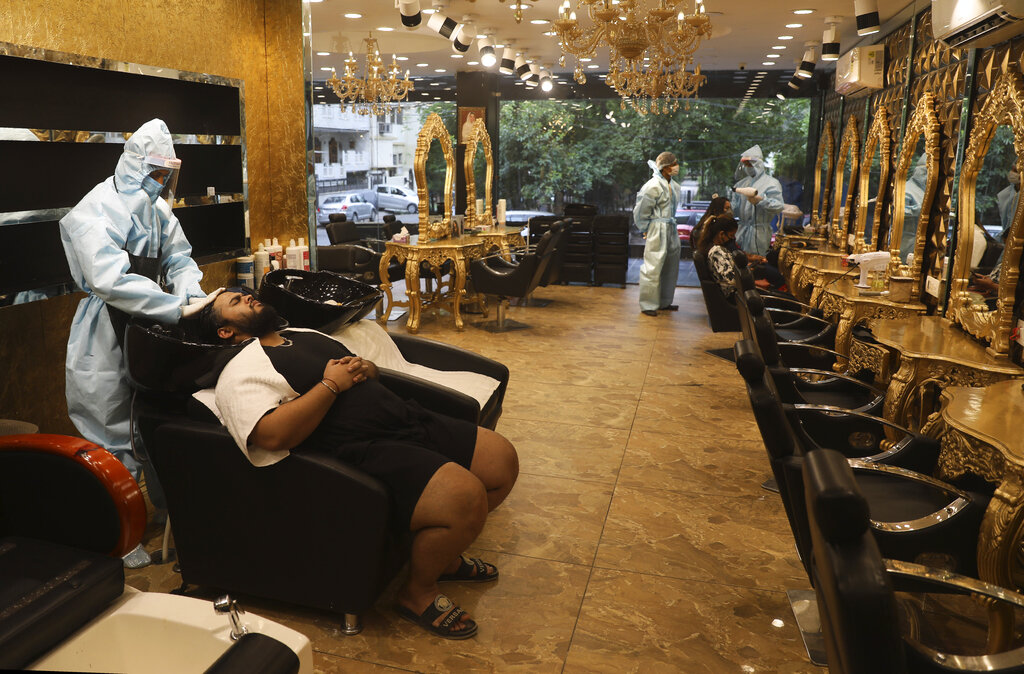 A hairdresser in personal protective suit attends to a customer at a hair salon in New Delhi, India, Friday, June 5, 2020.