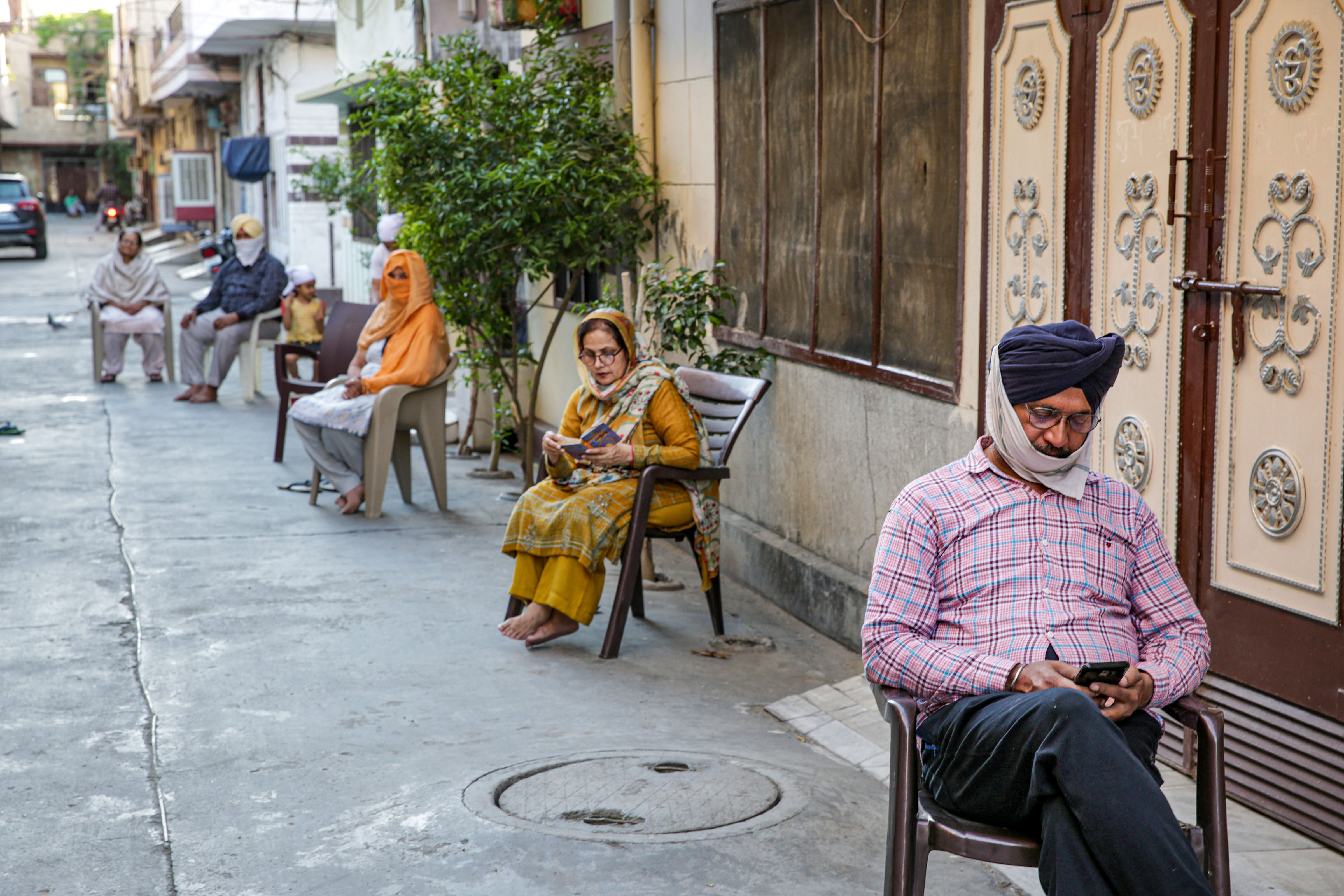 People maintain social distance as they read holy scriptures sitting outside their homes during lockdown amid coronavirus outbreak, in Amritsar, Thursday, April 2, 2020