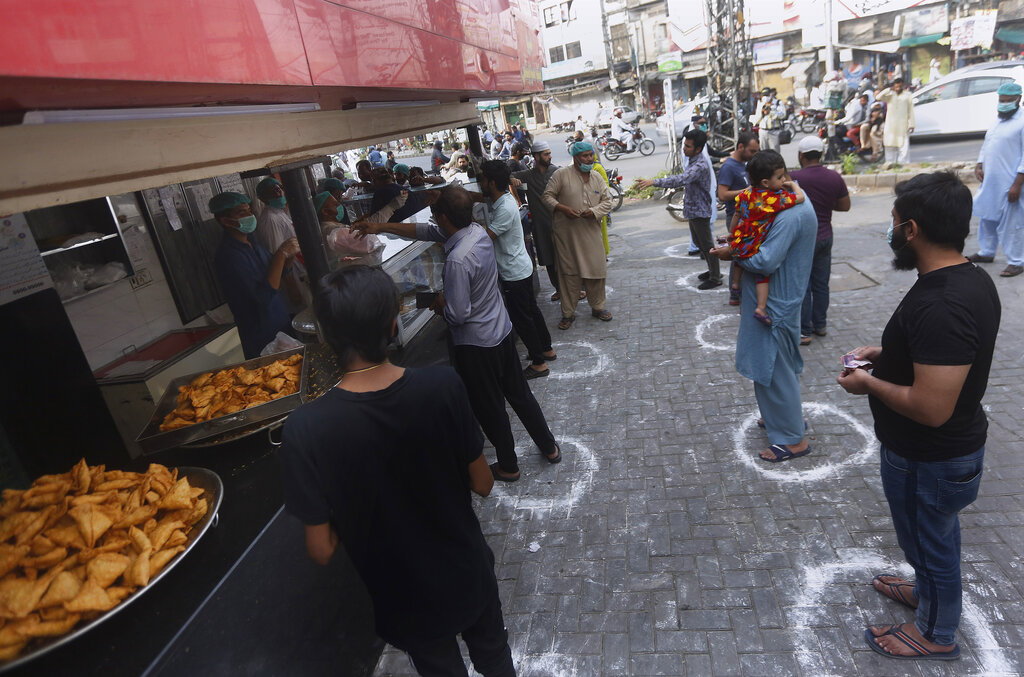 People maintaining a level of social distancing wait their turn to get traditional food from a bakery to break their fast on the first day of Ramadan, in Lahore, Pakistan. Saturday, April 25, 2020.