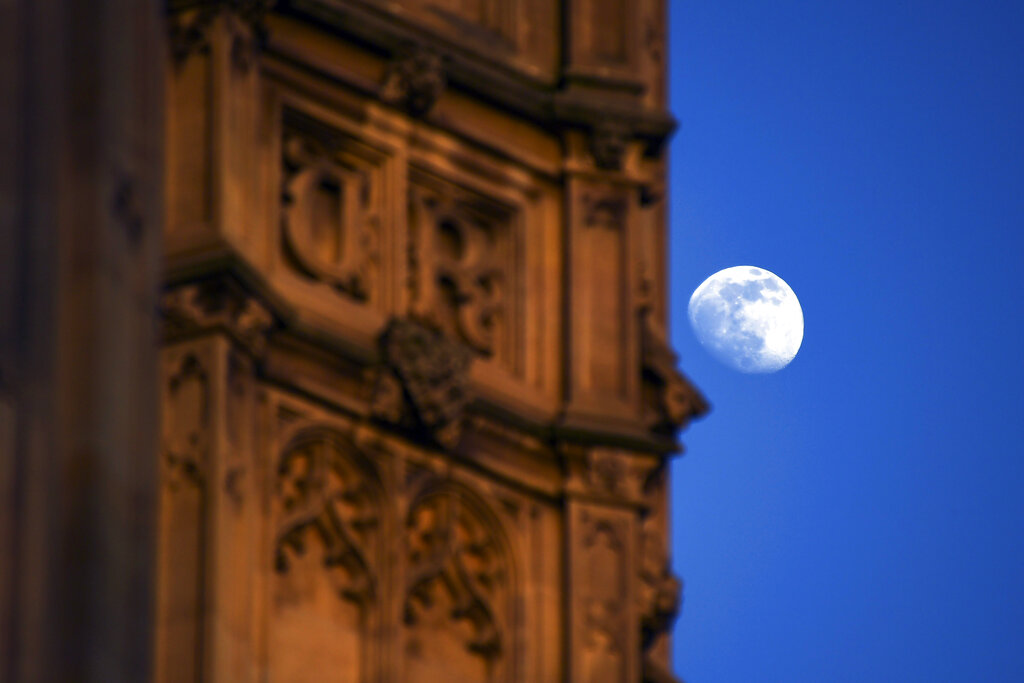 The moon rises behind the Victoria Tower in Westminster, in London, Friday, March 6, 2020