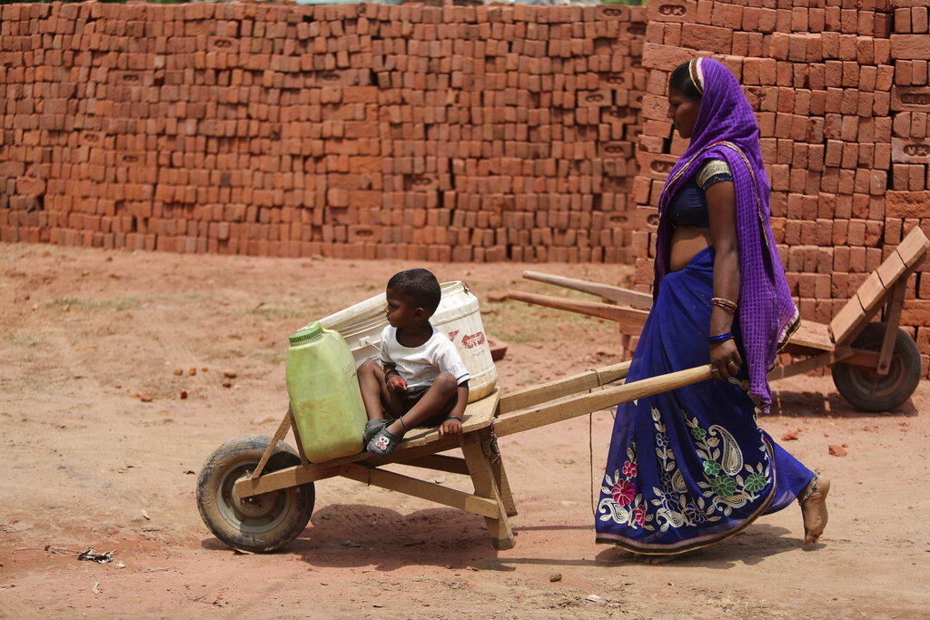 A woman pushes a cart with her child as she works at a brick kiln during lockdown to curb the spread of new coronavirus on the outskirts of Jammu, Sunday, May 10, 2020.