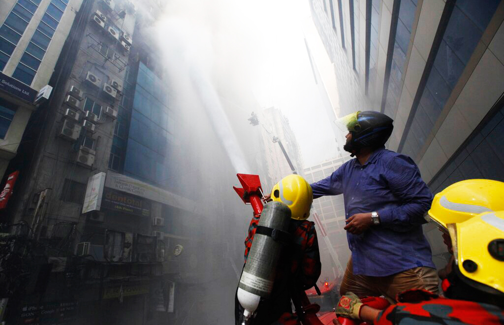 A commuter watches firefighters work to douse a fire in a multi-storied office building in Dhaka, Bangladesh, on Thursday