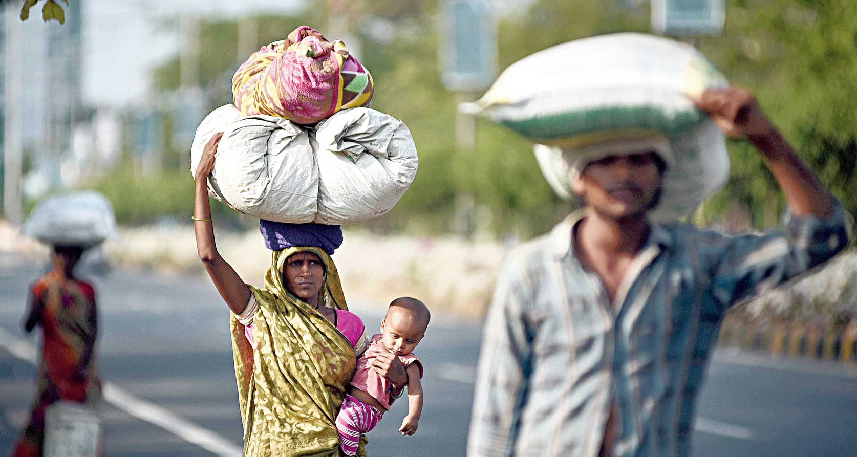 A migrant woman carrying her child walks along a road with her family in Vijaywada, Andhra Pradesh, on Wednesday to reach their native place in Maharashtra. 