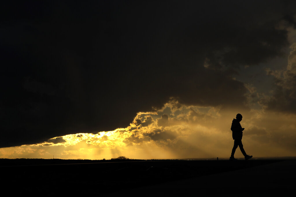 Aliyah Mosby is silhouetted against the sunset as she walks at the Liberty Memorial Thursday, March 19, 2020, in Kansas City, Mo. Mosby was taking advantage of warm weather on the first day of spring to get some fresh air as most of the community isolates to limit the spread of the coronavirus.
