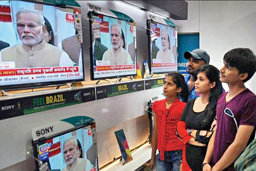 A crowd watches Narendra Modi give a speech on television.