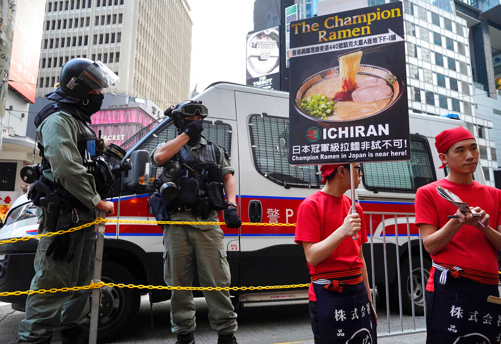 Riot police stand near workers advertising a noodle shop in Hong Kong on December 26
