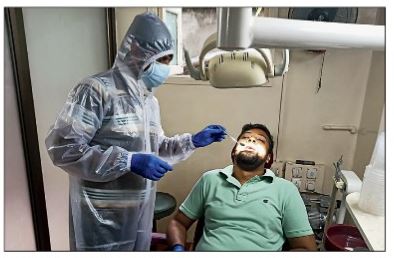 CD Block dentist Santanu Roy examines a patient wearing PPE, gloves and mask that he had to arrange before reopening his clinic