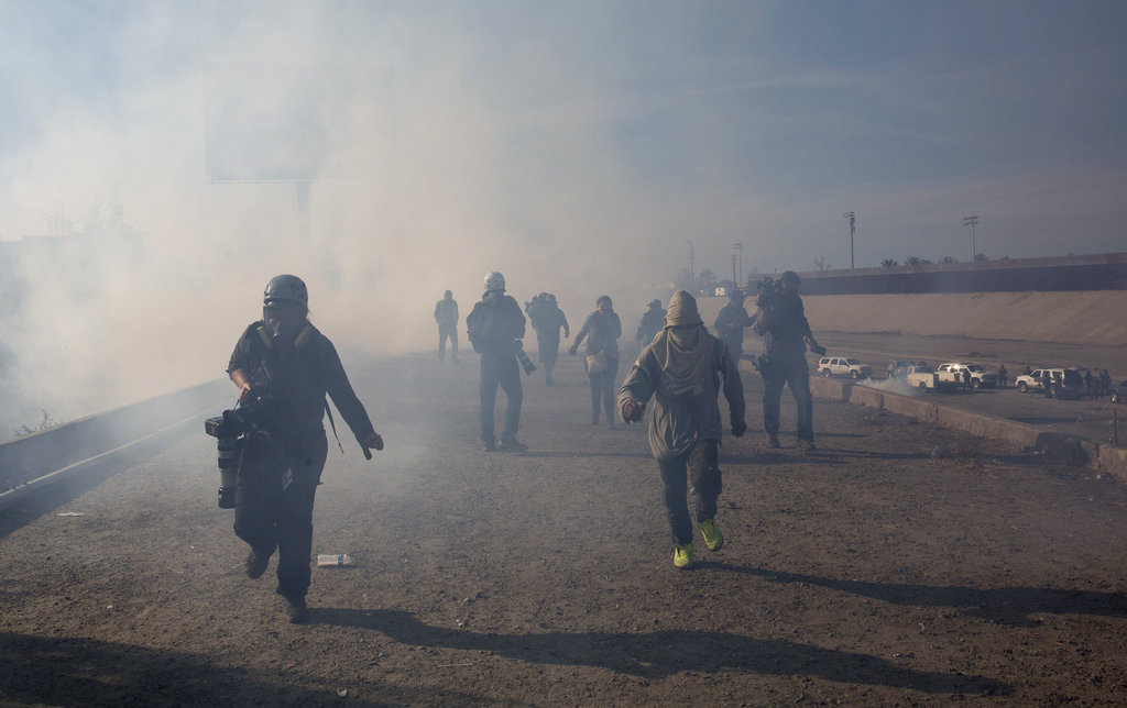 Migrants run from tear gas launched by US agents, amid photojournalists covering the Mexico-US border, after a group of migrants got past Mexican police at the Chaparral crossing in Tijuana, Mexico, on Sunday.