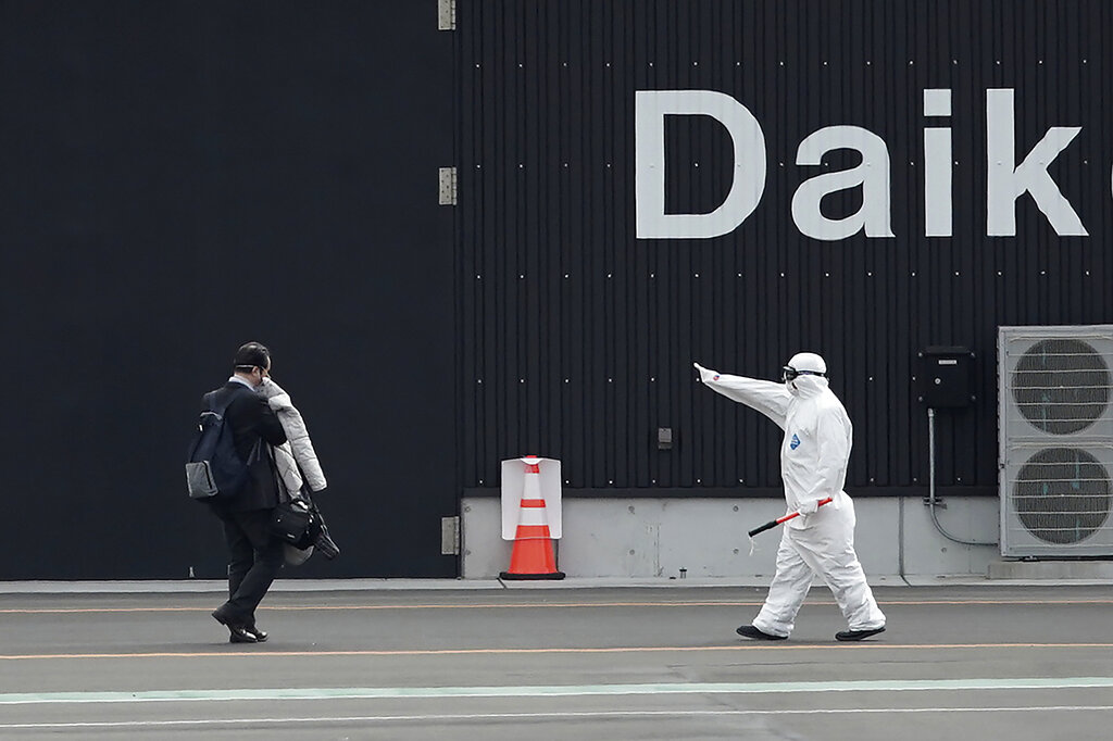 One of passengers, left, from the quarantined Diamond Princess cruise ship is guided after walking out from the ship at a port in Yokohama, near Tokyo, Wednesday