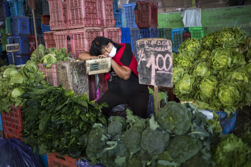 Kathy Velazquez, wearing a protective face mask as a precaution against the new coronavirus, naps in her vegetable stall as she waits for customers in Lima, Peru, Saturday, April 11, 2020.
