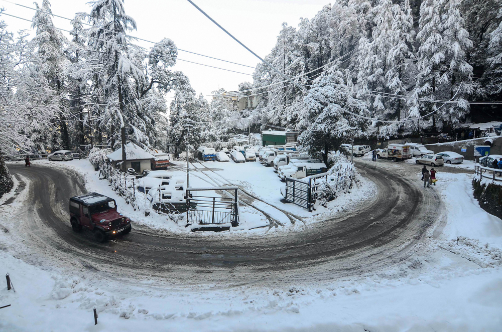 A jeep moves on a snow-covered road after snowfall in Shimla on December 14