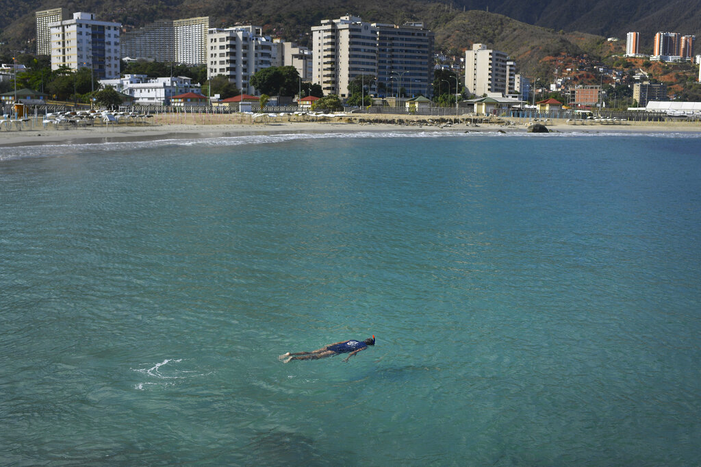 A man swims in the normally crowded popular beach Los Corales, in La Guaira, Venezuela, Saturday, March 21, 2020. Most people are staying home after nonessential activities were cancelled due to the COVID-19 pandemic.