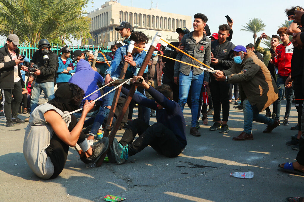 Anti-government protesters use a slingshot to fire a stone at security forces during clashes in Baghdad, Iraq, on Thursday