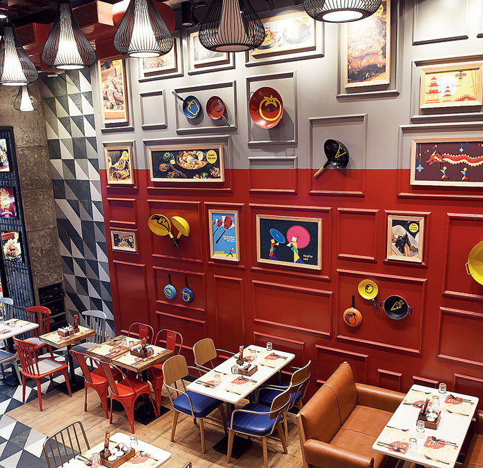 As you walk in, the first thing that catches your eye is the height of the ceiling and a red-and-grey wall with quirky elements like colourful posters and hand-painted pots and pans in vibrant hues. Use of leather and metal in the couches and chairs adds an extra touch of cool.