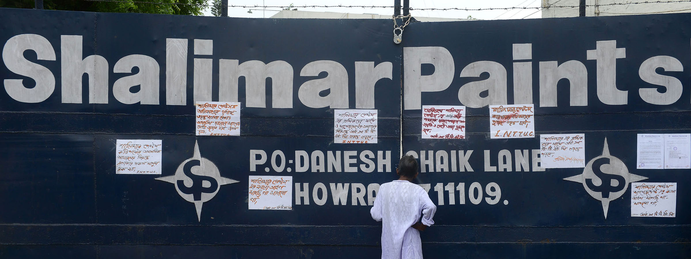 A Man peeps through the gates of a closed Shalimar Paints factory in Howrah.