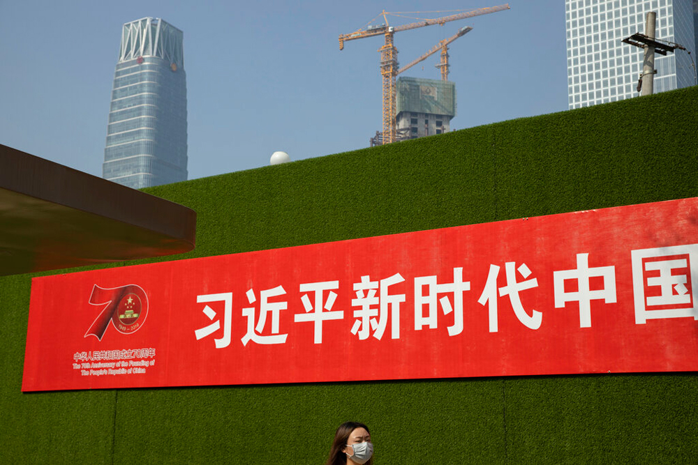 A woman wearing a mask walks past by a slogan, 'Xi Jinping, New Era China',  on Friday