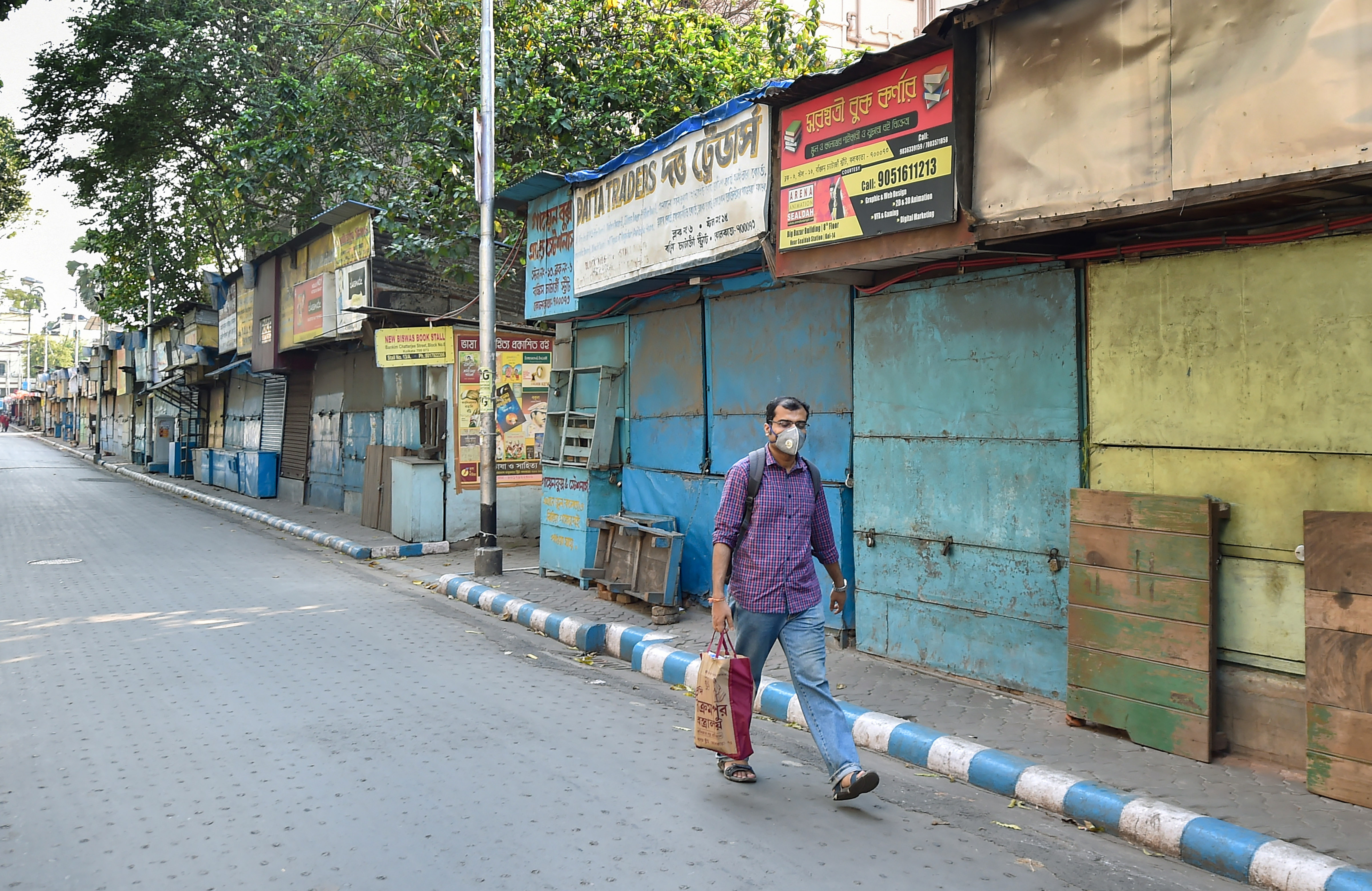 A man wears a mask and walks past a closed market before lockdown in the wake of coronavirus pandemic in Kolkata, Monday, March 23, 2020.
